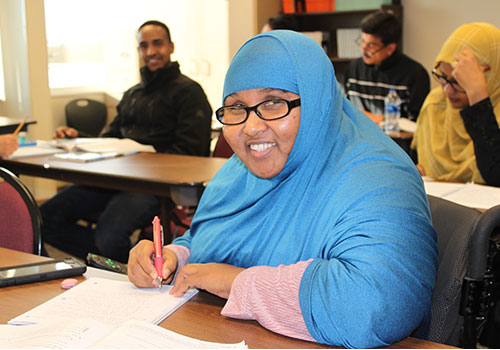 A female student in a khimar studies in a classroom with other students