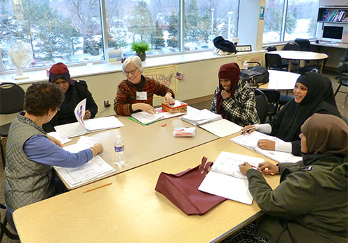 Students around a table in a classroom, learning with a teacher