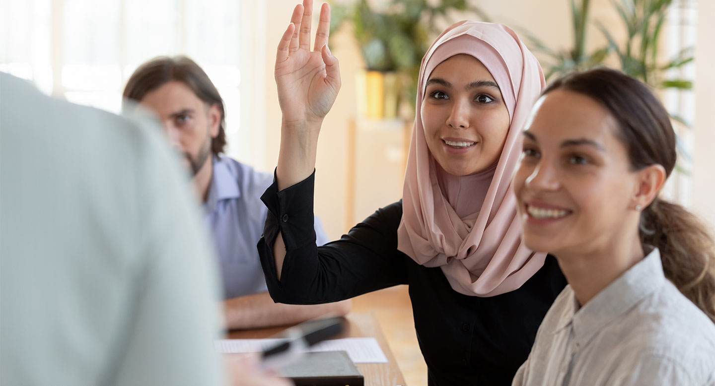 A student in a hijab raises her hand